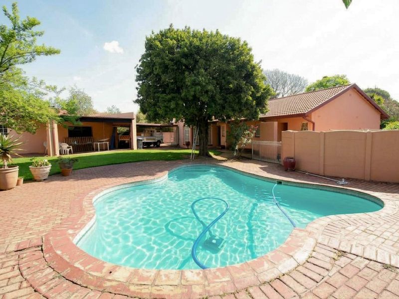 A backyard area featuring a swimming pool with brick paving, a covered patio, and a boundary wall.