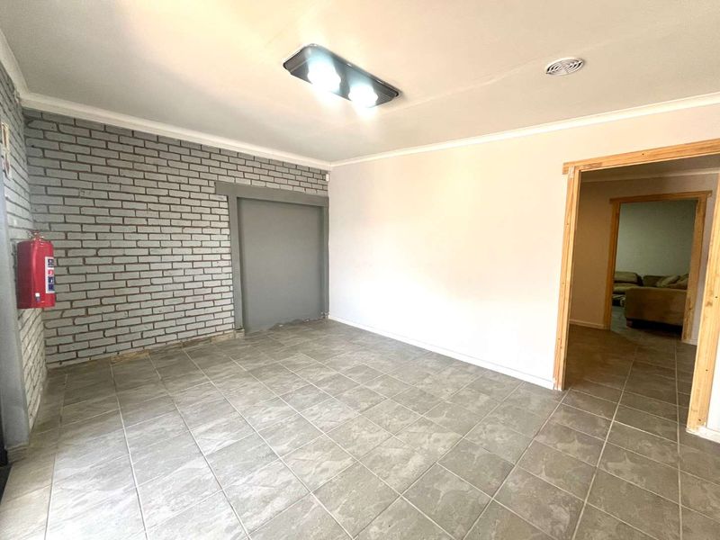 An empty living area featuring tiled flooring, an exposed brick feature wall, and a doorway leading to an adjacent room.