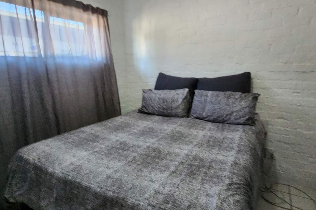 A bedroom featuring a painted brick wall and a window with installed curtain tracks.