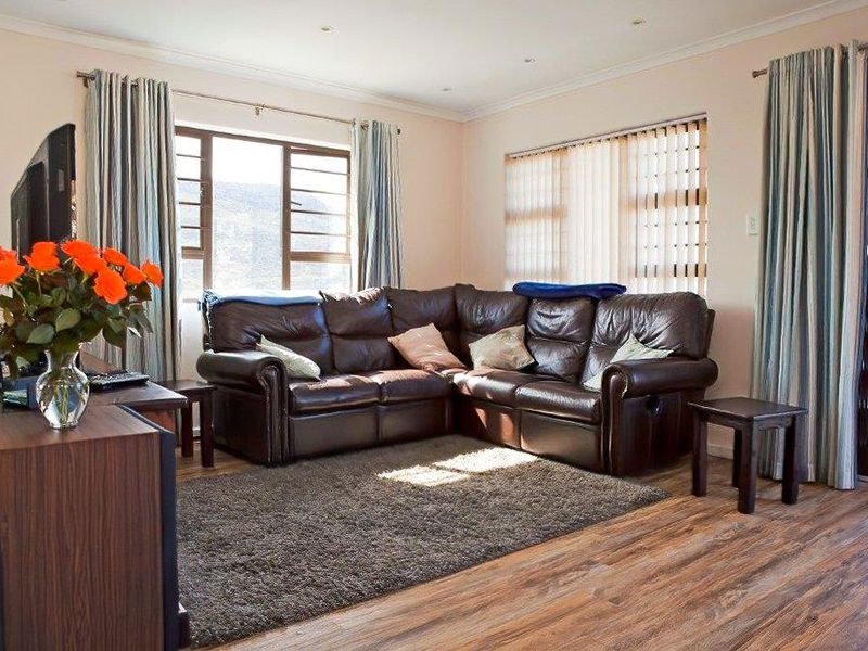 A comfortable living room featuring laminate flooring, recessed downlighting, and large windows with access to an outdoor area.