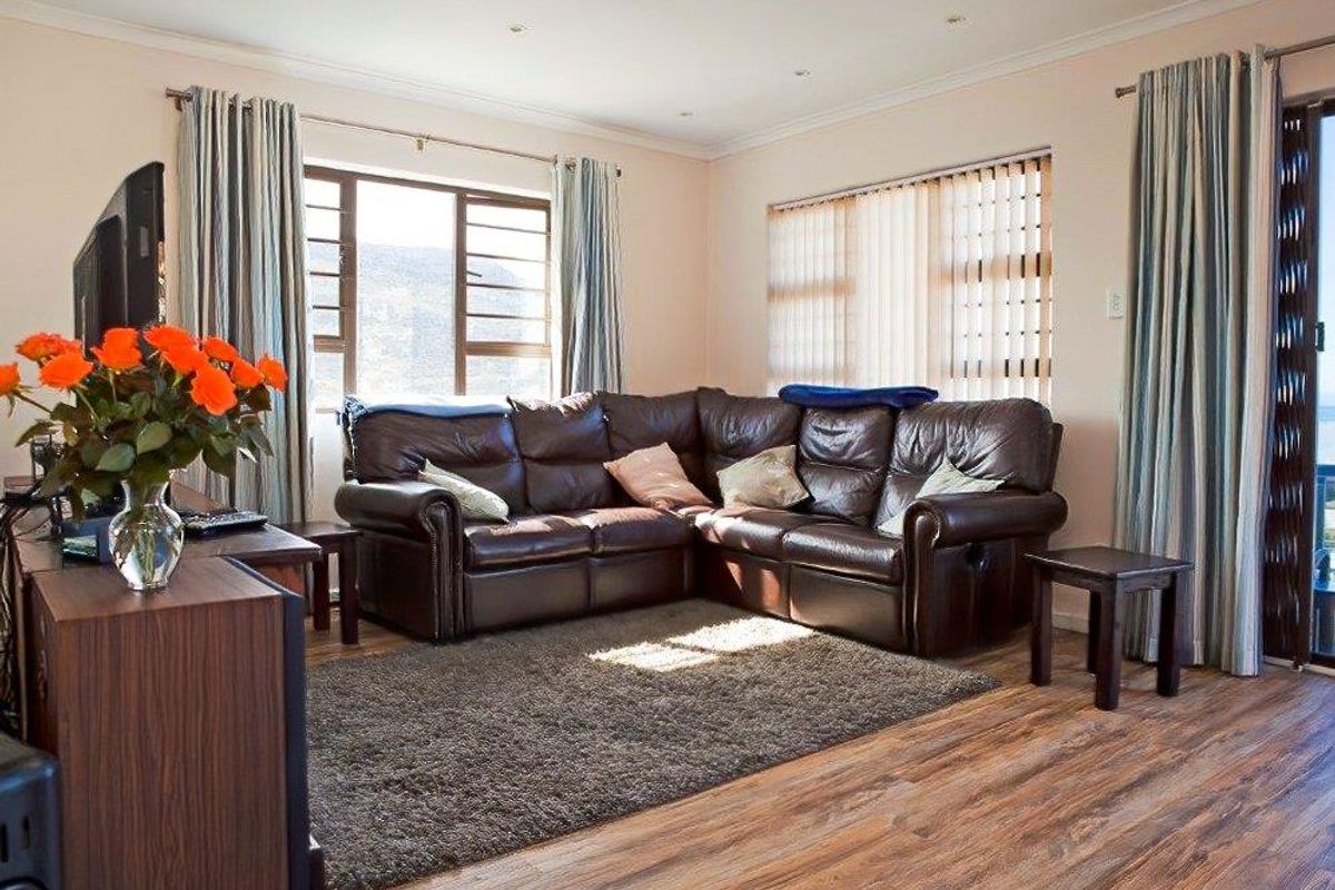 A comfortable living room featuring laminate flooring, recessed downlighting, and large windows with access to an outdoor area.