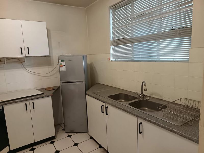 A functional kitchen featuring white cabinetry, laminate countertops, a double bowl stainless steel sink, and tiled backsplash with a window providing natural light.