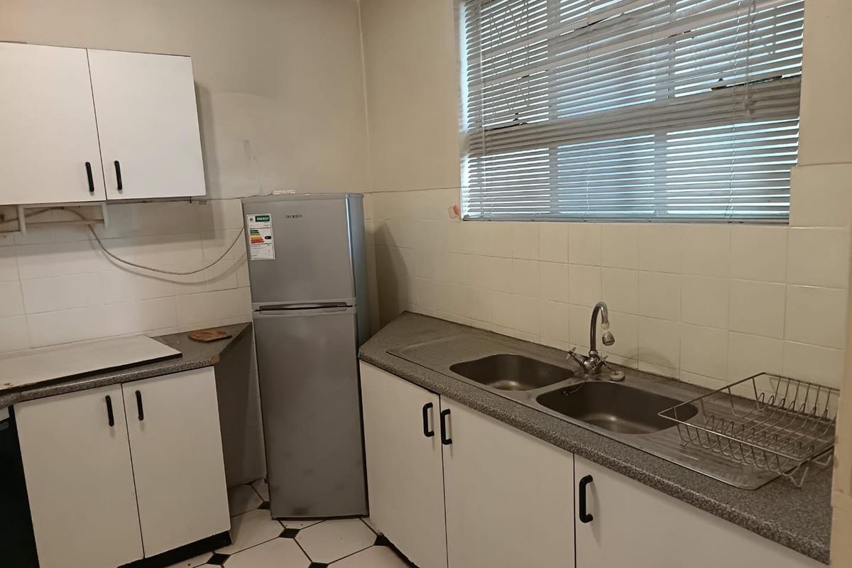 A functional kitchen featuring white cabinetry, laminate countertops, a double bowl stainless steel sink, and tiled backsplash with a window providing natural light.