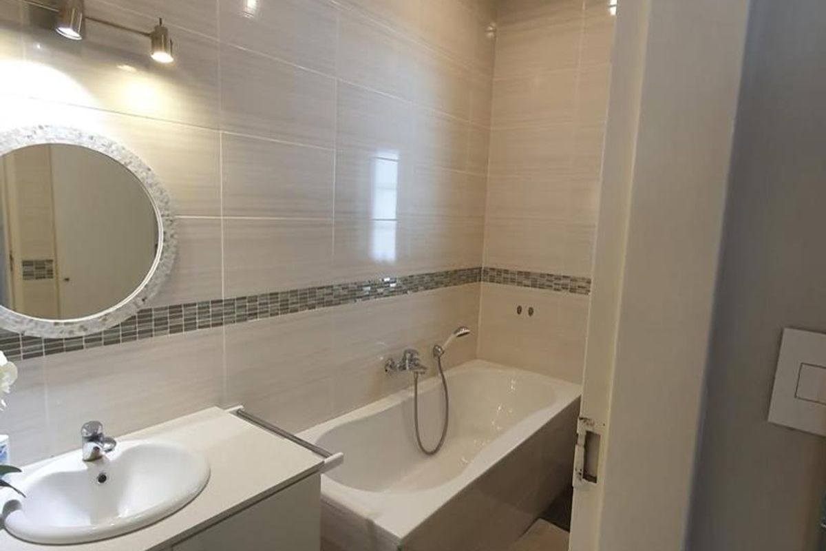 A well-maintained bathroom featuring a built-in vanity with integrated basin, a bathtub with shower mixer, and neutral wall tiling with a decorative mosaic border.