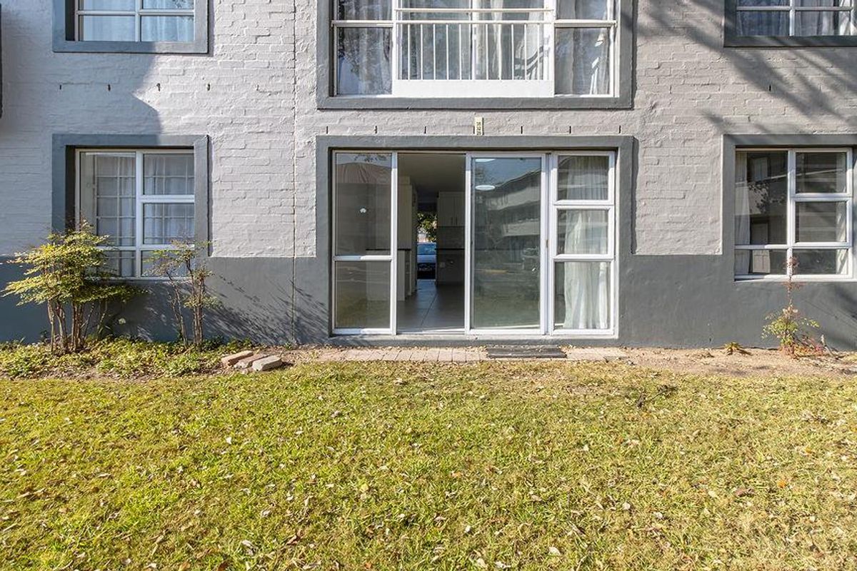Rear exterior view of the apartment building featuring a brick facade, sliding glass door access, and a small garden area.
