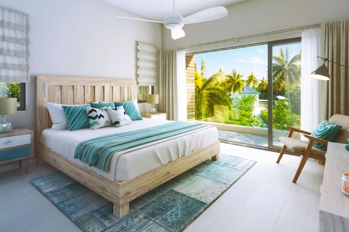 A bright, modern bedroom featuring a ceiling fan and large sliding glass doors that open onto a private balcony with tropical views.
