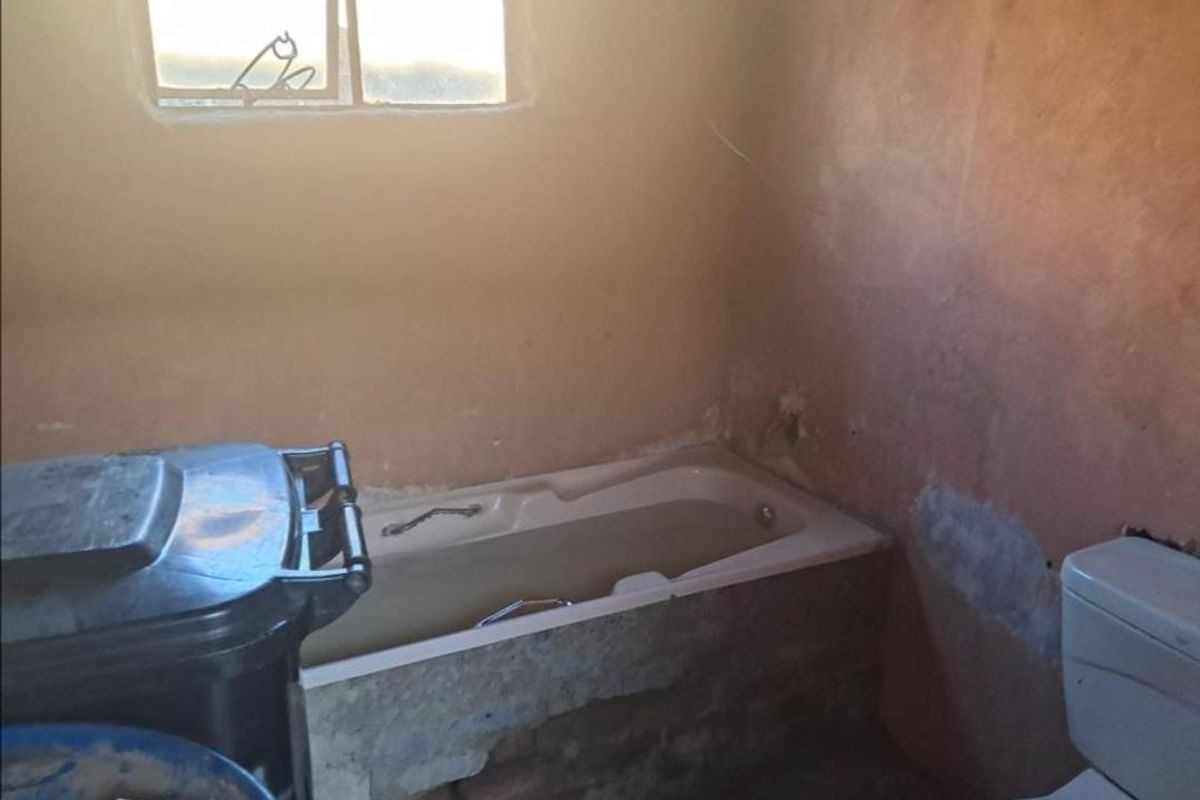 A bathroom in need of significant renovation, featuring a built-in bathtub and toilet with visible wall damage and exposed brickwork.