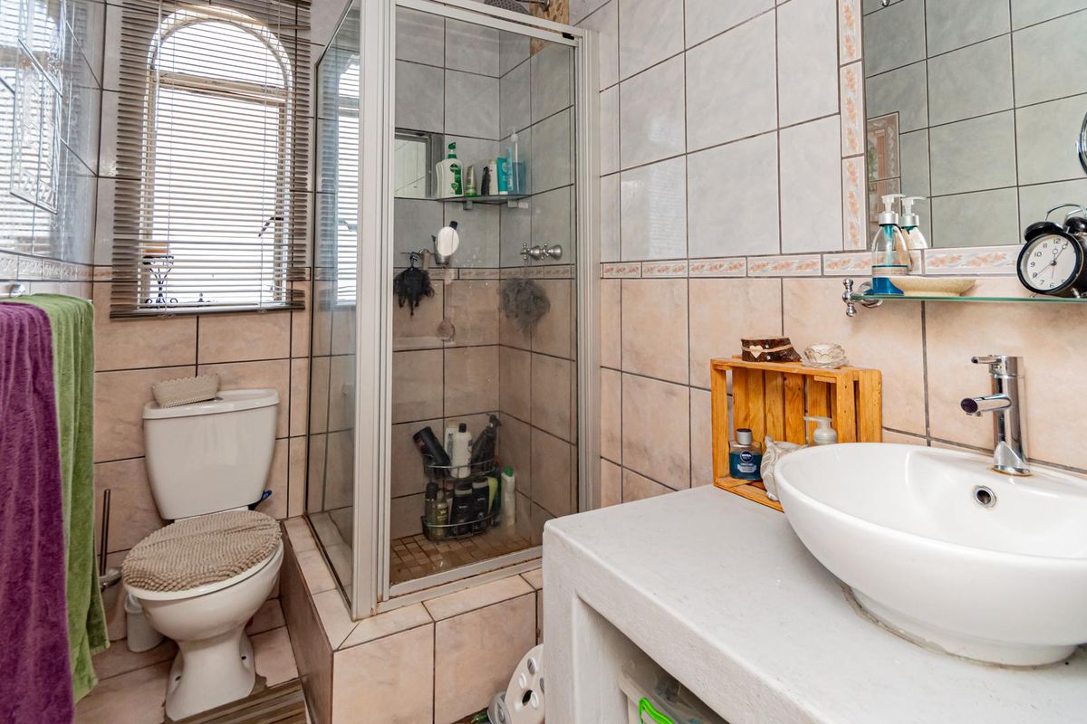 A compact bathroom featuring a glass-enclosed shower, a raised vanity with a vessel sink, and a standard toilet with tiled walls.