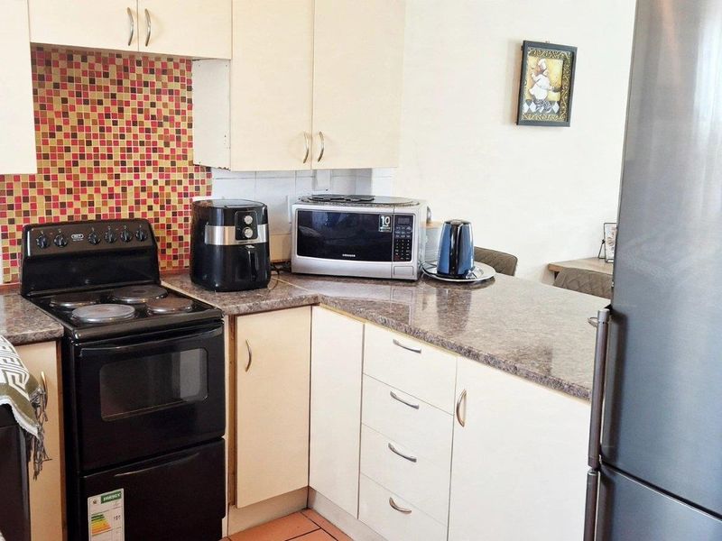 A functional kitchen featuring light-toned cabinetry, granite-look laminate countertops, a vibrant mosaic tile backsplash, and a freestanding stove.