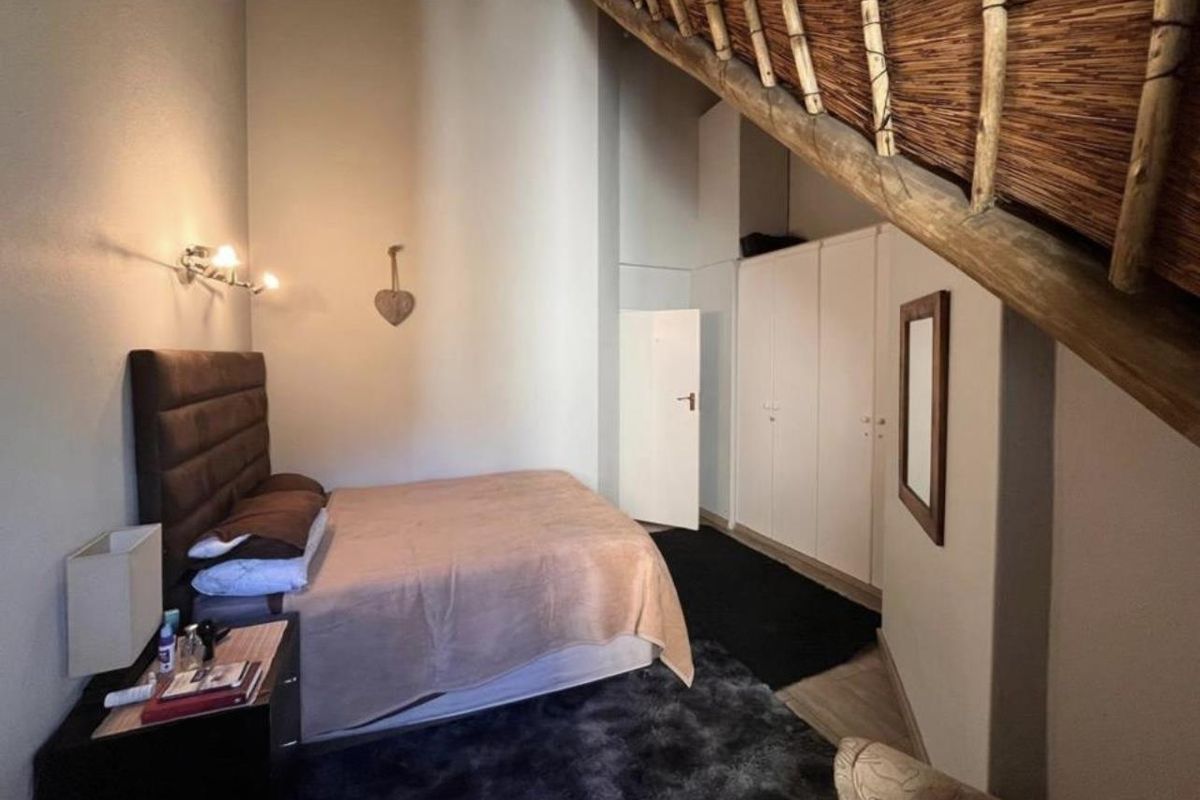 A bedroom featuring built-in cupboards and a unique sloped ceiling design with exposed thatch detailing.