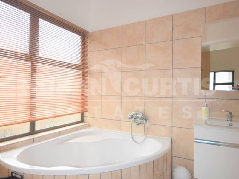 Bathroom featuring a corner bathtub, wall-mounted vanity, and neutral wall tiling. The space offers a functional layout with natural light from the window.