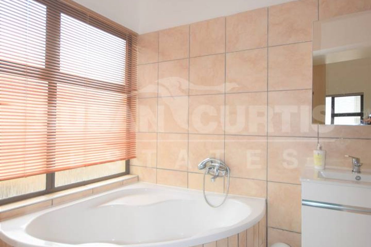 Bathroom featuring a corner bathtub, wall-mounted vanity, and neutral wall tiling. The space offers a functional layout with natural light from the window.