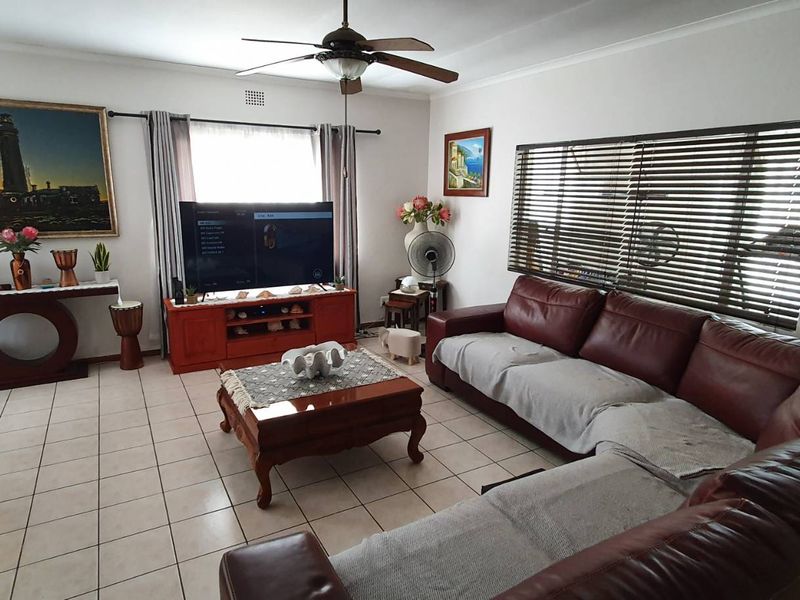 A spacious living room featuring tiled flooring, a ceiling fan, and large windows with venetian blinds, offering a comfortable and functional living space.