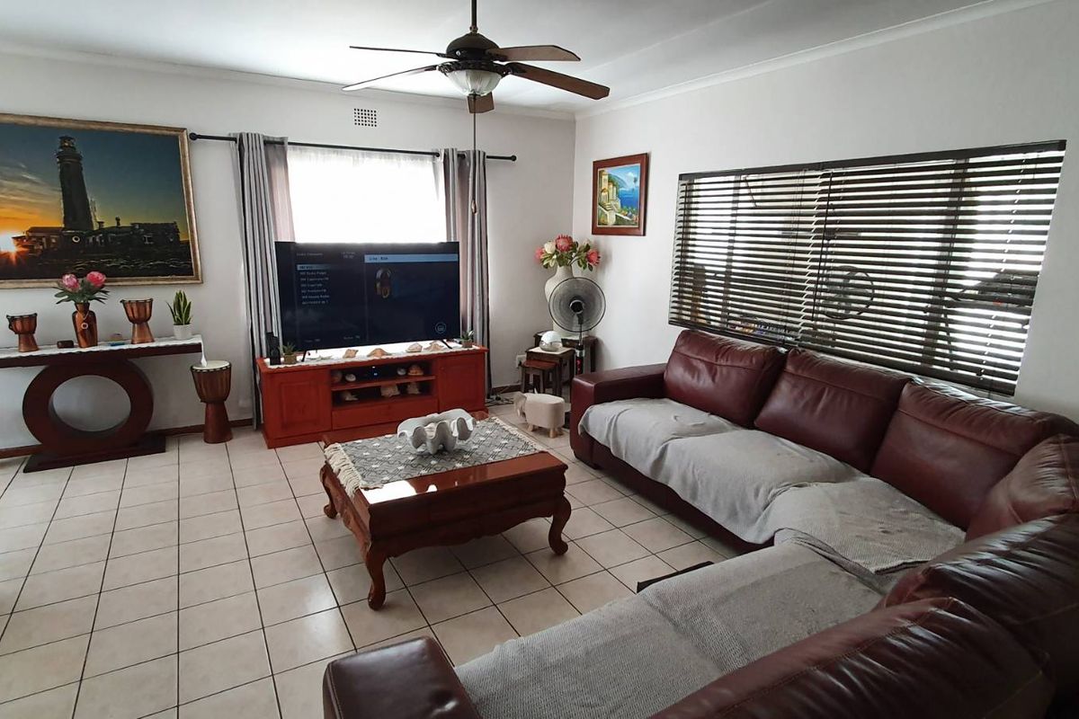 A spacious living room featuring tiled flooring, a ceiling fan, and large windows with venetian blinds, offering a comfortable and functional living space.