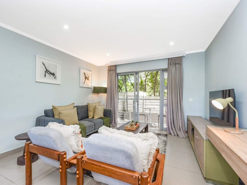 A bright and well-maintained living room featuring tiled flooring, recessed downlights, and a sliding glass door providing access to the outdoor area.