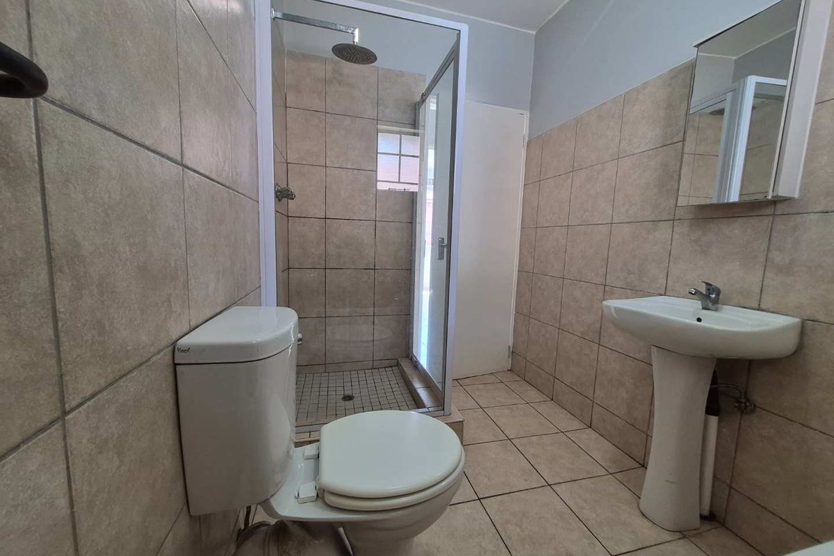 A functional bathroom featuring a pedestal basin, toilet, and a glass-enclosed shower with a rain shower head, finished with neutral wall and floor tiling.
