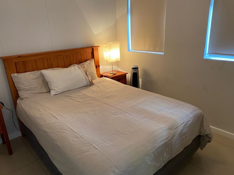 A functional bedroom featuring tiled flooring and dual windows fitted with roller blinds.