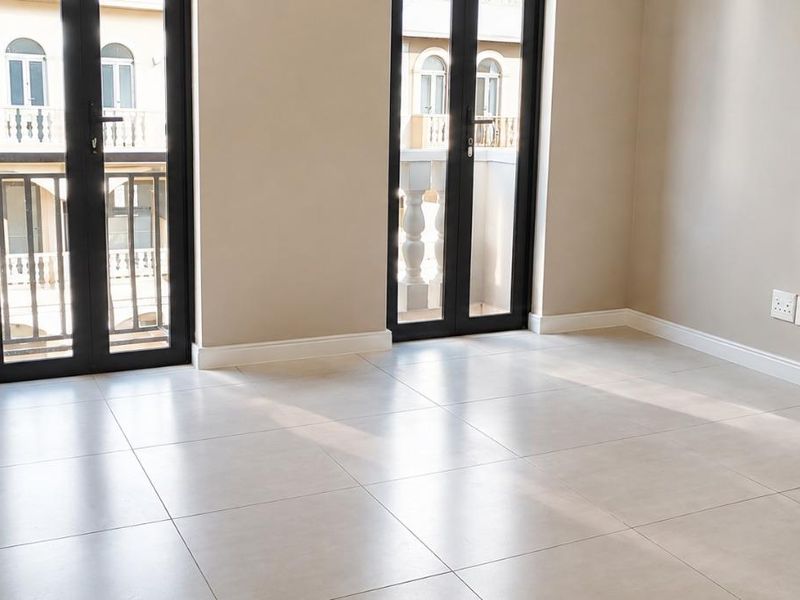 A bright, empty bedroom featuring neutral tiled flooring, built-in cupboards, and double french doors leading to a balcony.