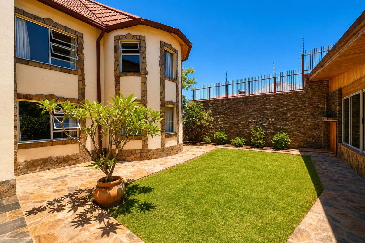 A well-maintained rear garden featuring a manicured lawn, stone-paved patio area, and stone-clad exterior walls with secure perimeter fencing.