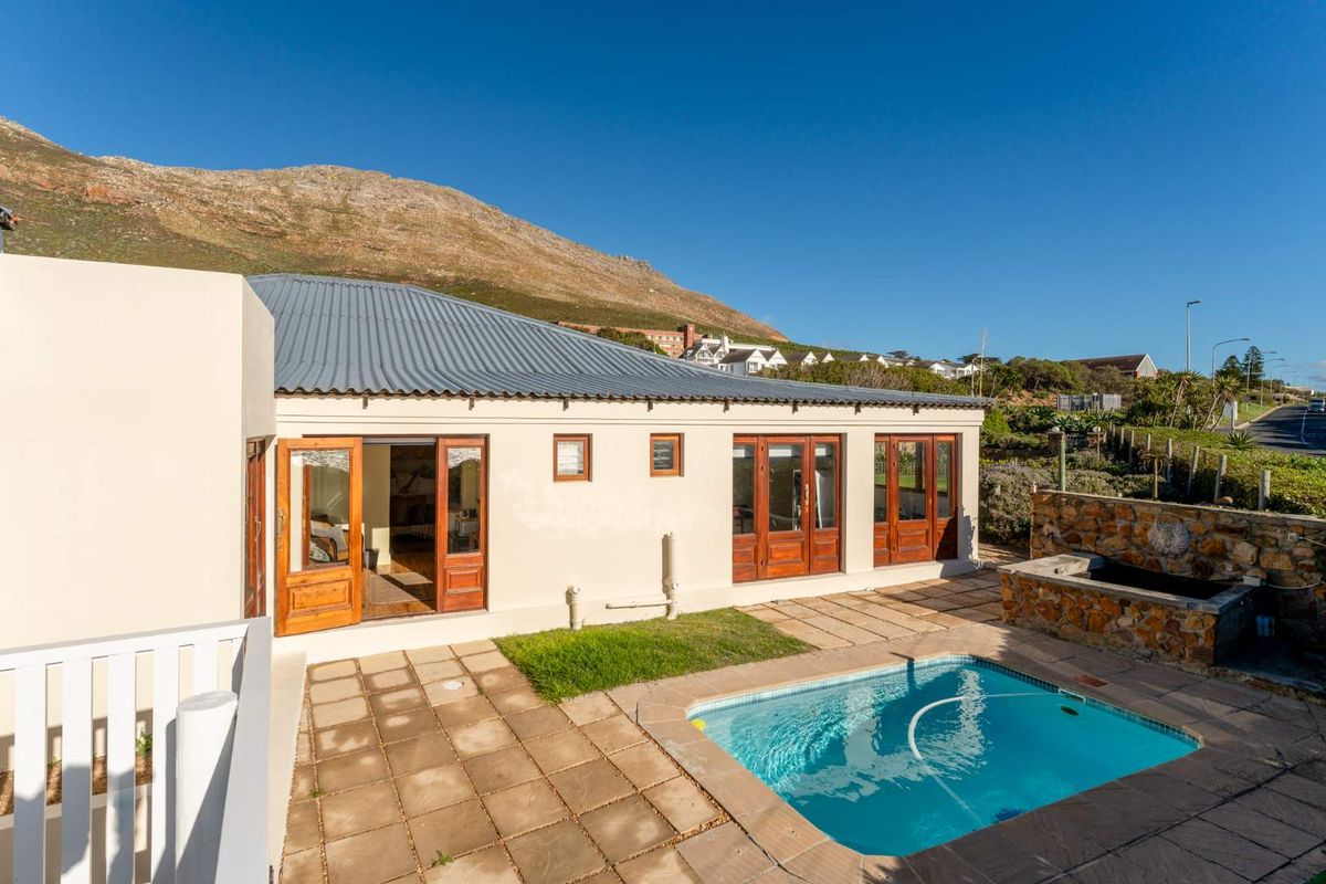 Rear exterior view featuring a swimming pool, stone-clad water feature, paved patio area, and timber-framed glass doors leading into the home.