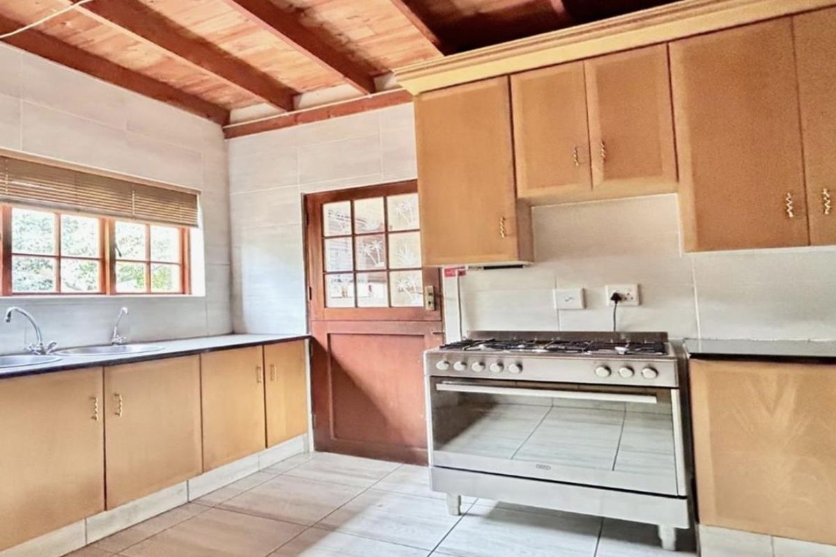 A functional kitchen featuring wooden cabinetry, tiled flooring, exposed timber ceiling beams, and a freestanding gas stove with oven.