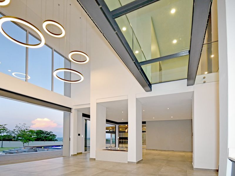 Spacious open-plan living area featuring double-volume ceilings, a large glass skylight, modern pendant lighting, and seamless indoor-outdoor flow through stacking glass doors.