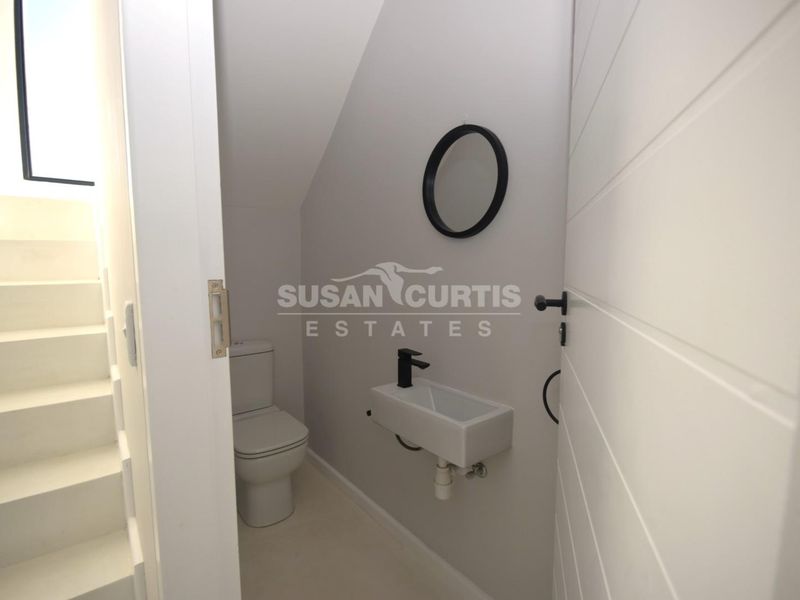 A modern, compact guest bathroom featuring a wall-mounted basin with a black mixer tap and a sleek toilet, finished in a neutral palette.