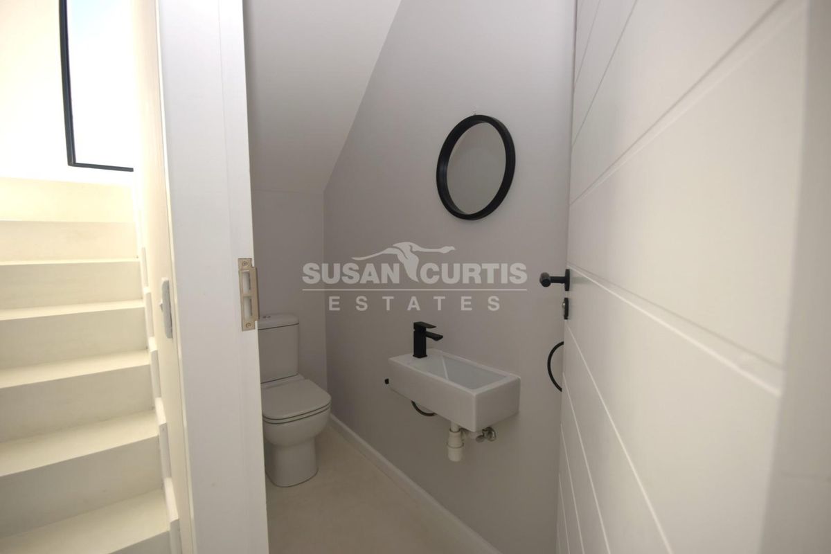 A modern, compact guest bathroom featuring a wall-mounted basin with a black mixer tap and a sleek toilet, finished in a neutral palette.