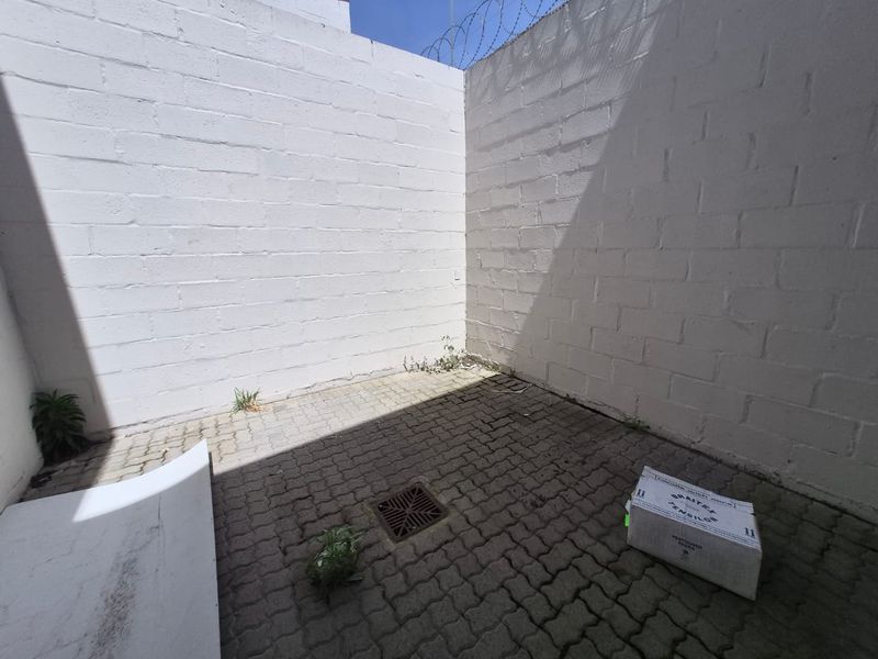 A small, enclosed rear courtyard area featuring concrete block walls, paved flooring with a drainage grate, and security razor wire.
