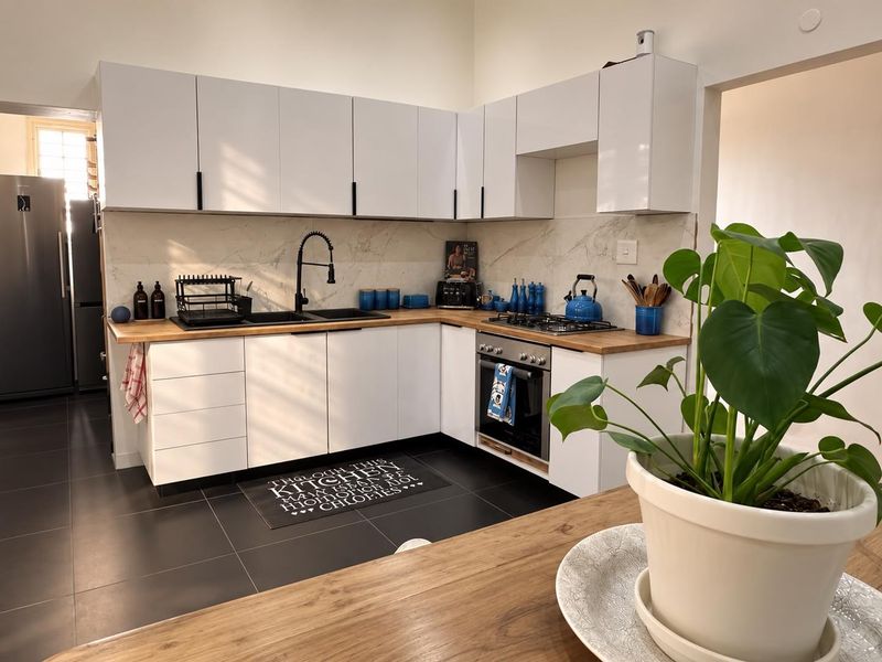 Modern kitchen featuring white cabinetry, wooden countertops, a stone-look backsplash, and integrated appliances, complemented by dark floor tiles.