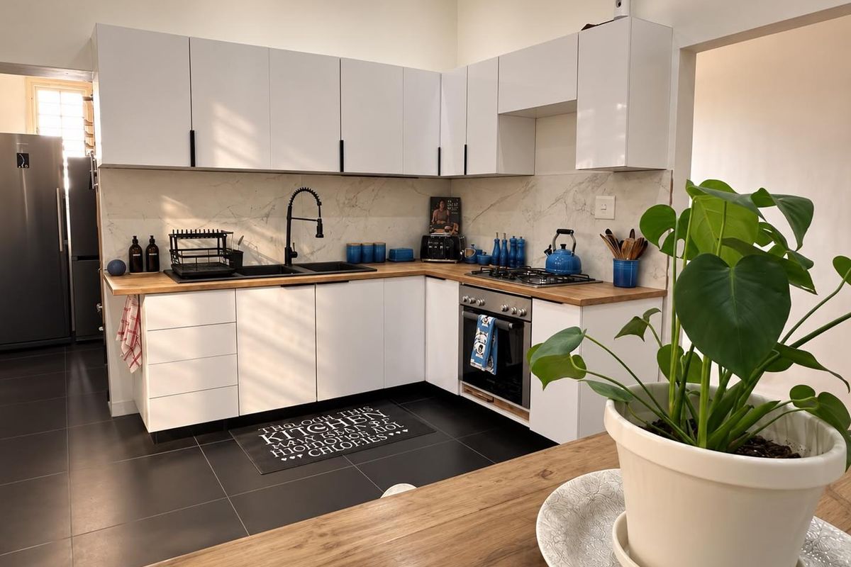 Modern kitchen featuring white cabinetry, wooden countertops, a stone-look backsplash, and integrated appliances, complemented by dark floor tiles.