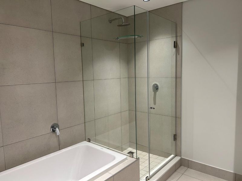 Modern bathroom featuring a built-in bathtub and a separate glass-enclosed shower with neutral ceramic tiling throughout.
