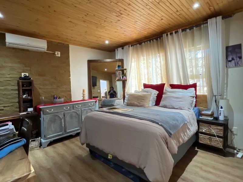 A cozy bedroom featuring a warm timber tongue and groove ceiling, a stone feature wall, and modern laminate flooring with an integrated air conditioning unit.