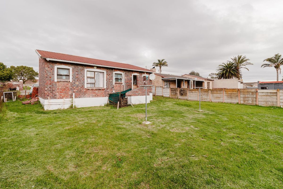 Rear view of a brick house featuring a spacious backyard, perimeter boundary wall, and metal washing line infrastructure.