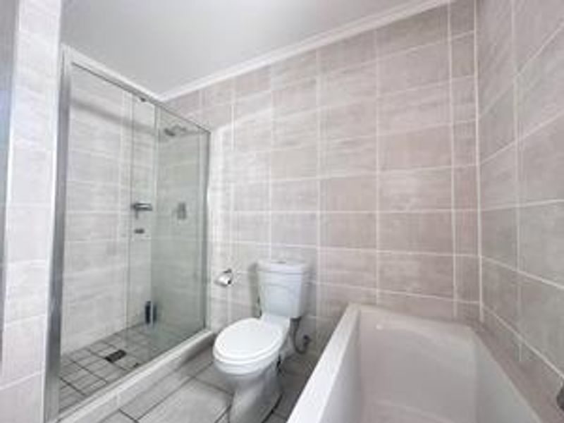 A clean, modern bathroom featuring a glass-enclosed shower, a separate bathtub, and neutral ceramic tiling throughout.