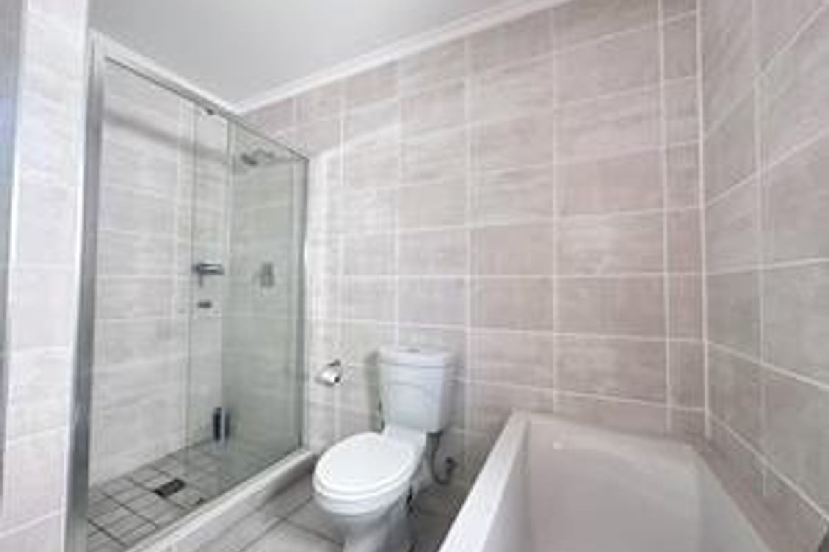 A clean, modern bathroom featuring a glass-enclosed shower, a separate bathtub, and neutral ceramic tiling throughout.