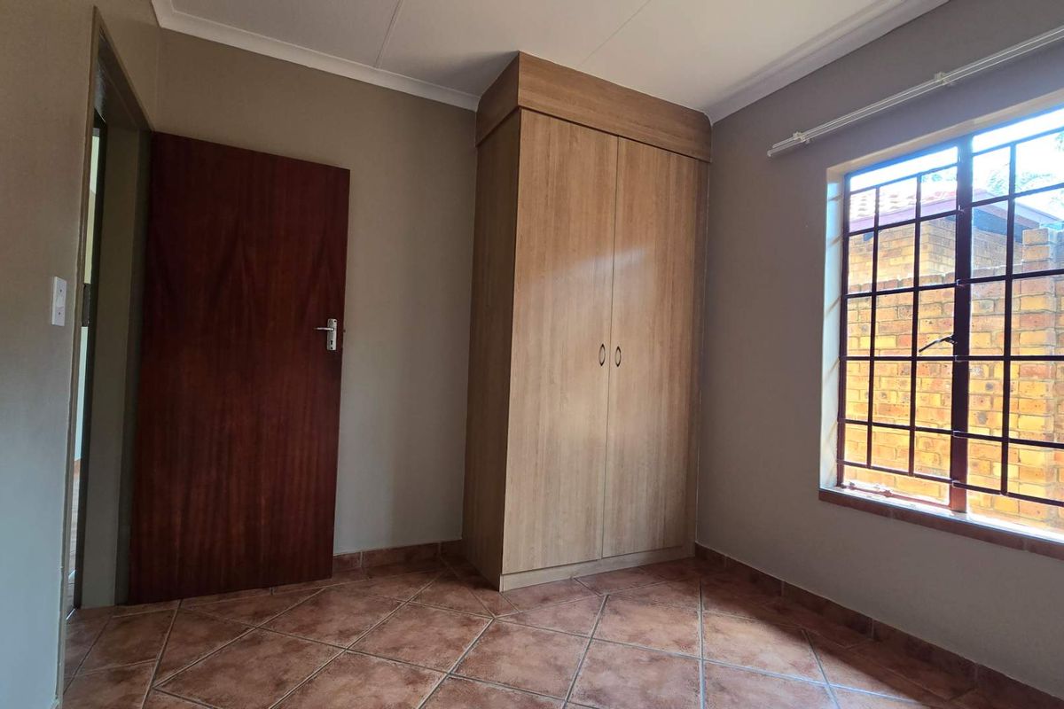 A bedroom featuring tiled flooring, a built-in wooden wardrobe, and a window with security bars.