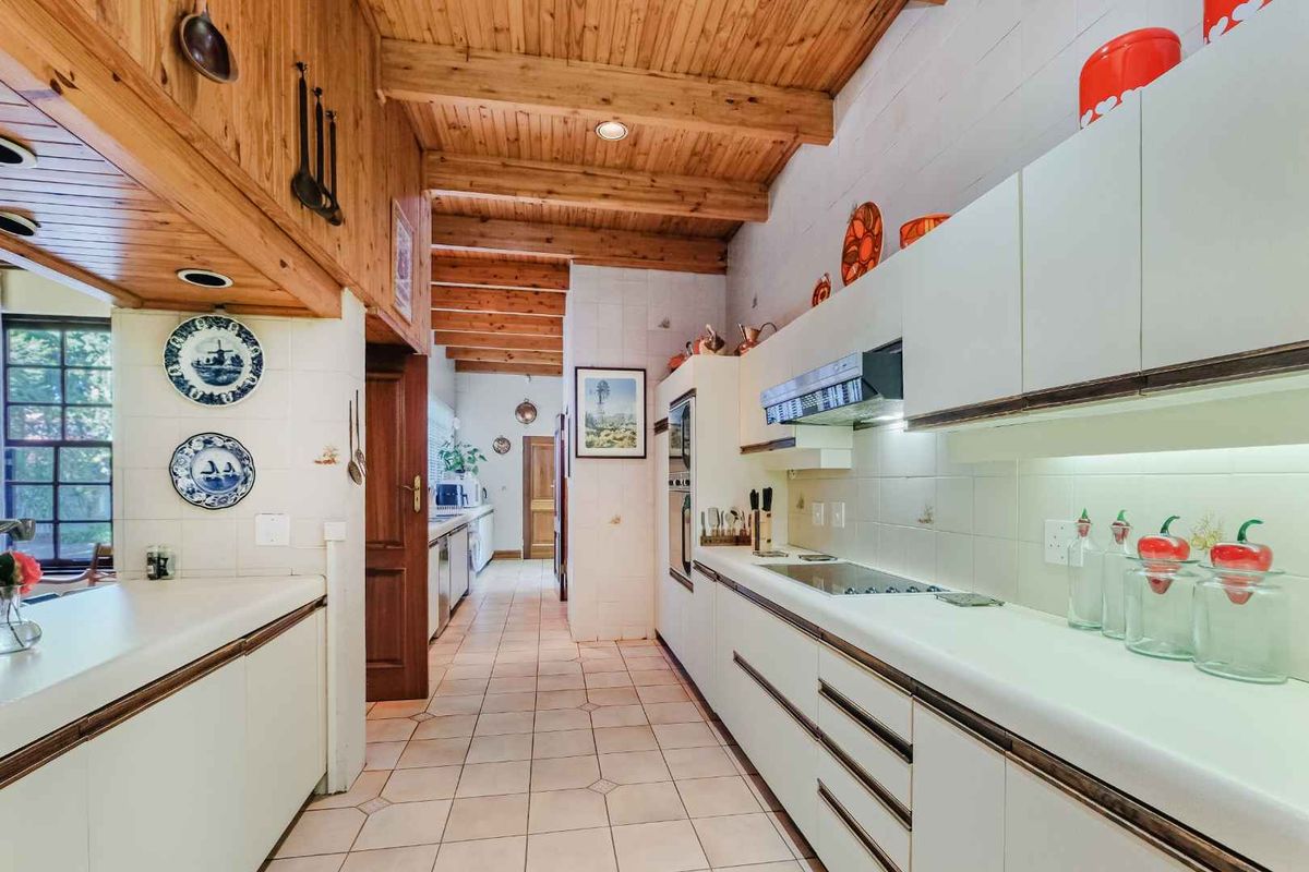 A functional kitchen featuring built-in cabinetry, integrated oven and hob, tiled flooring, and a distinctive exposed timber beam ceiling.
