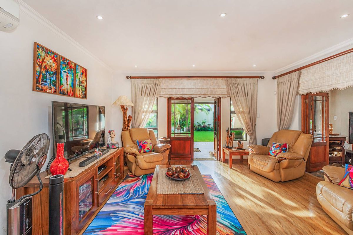A bright living room featuring wood-look flooring, recessed ceiling lighting, and double doors opening directly onto a private garden patio.
