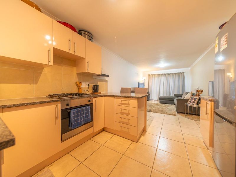 Open-plan kitchen and living area featuring light-toned cabinetry, granite countertops, built-in oven, gas hob, and tiled flooring throughout.