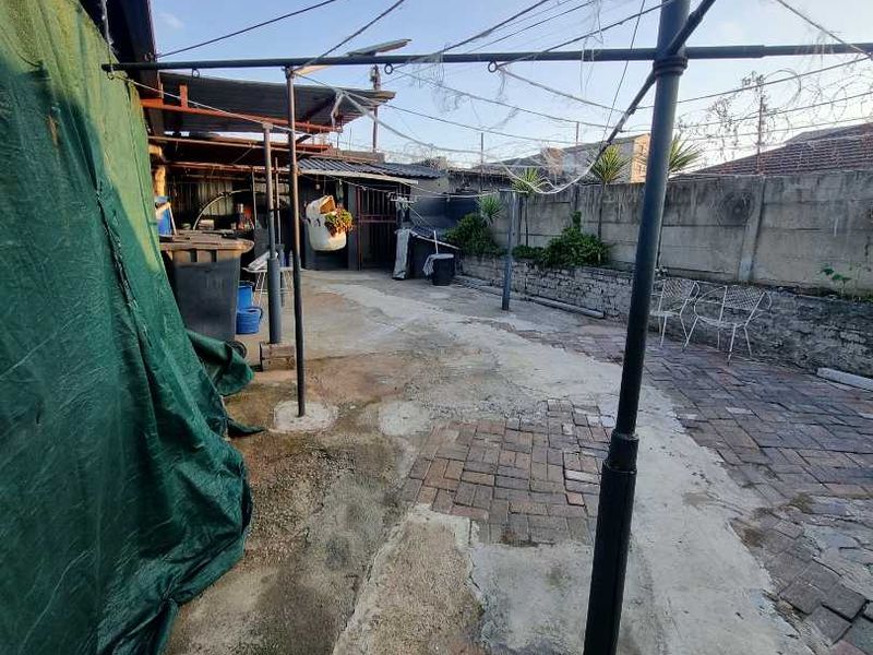 A rear outdoor area featuring a mix of concrete and brick paving, enclosed by a perimeter wall with a fixed metal clothesline structure.
