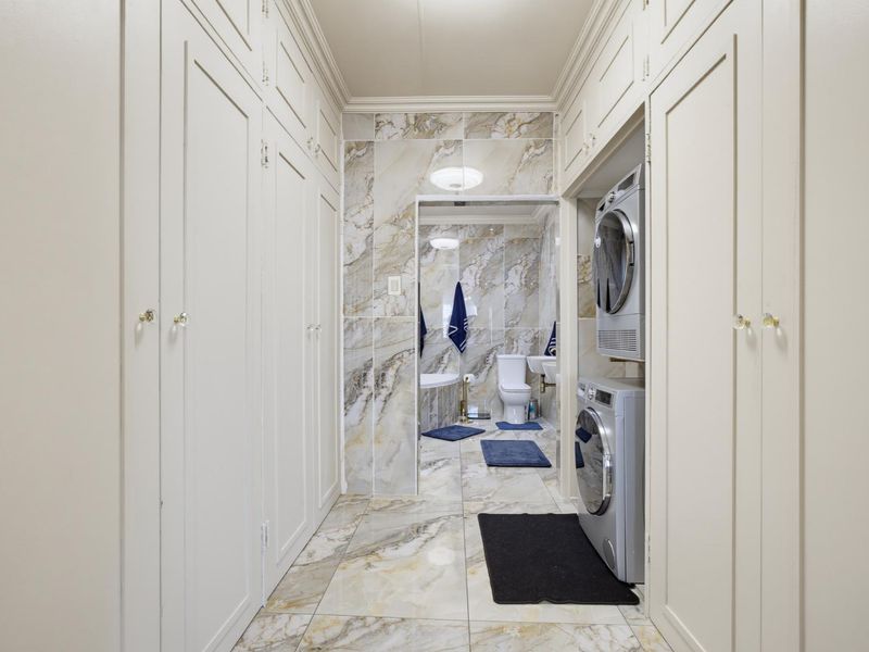 A well-appointed laundry area featuring extensive built-in cabinetry, marble-look tiling, and direct access to an adjoining bathroom.