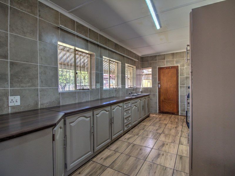 A functional kitchen featuring tiled walls, laminate countertops, built-in cabinetry, and wood-look tiled flooring with security bars on the windows.