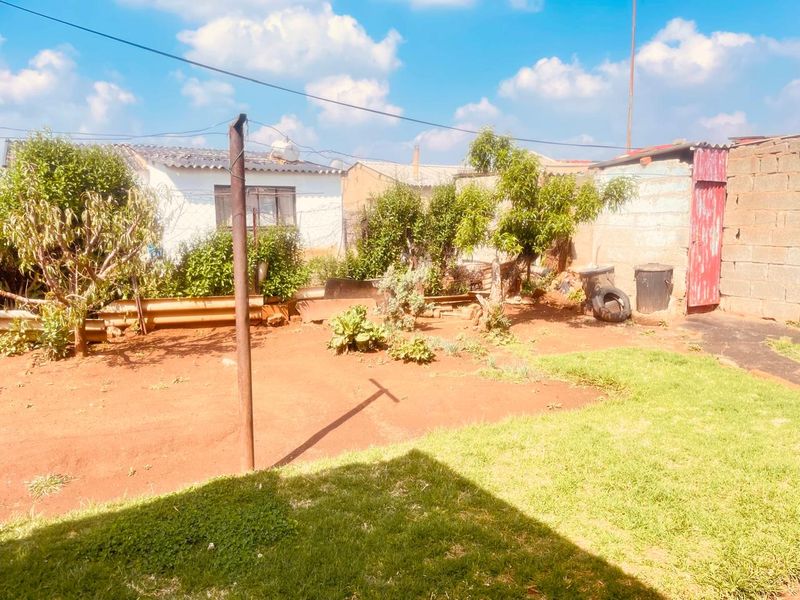 A rear exterior view of the property featuring an open garden area with boundary walls and a metal gate.