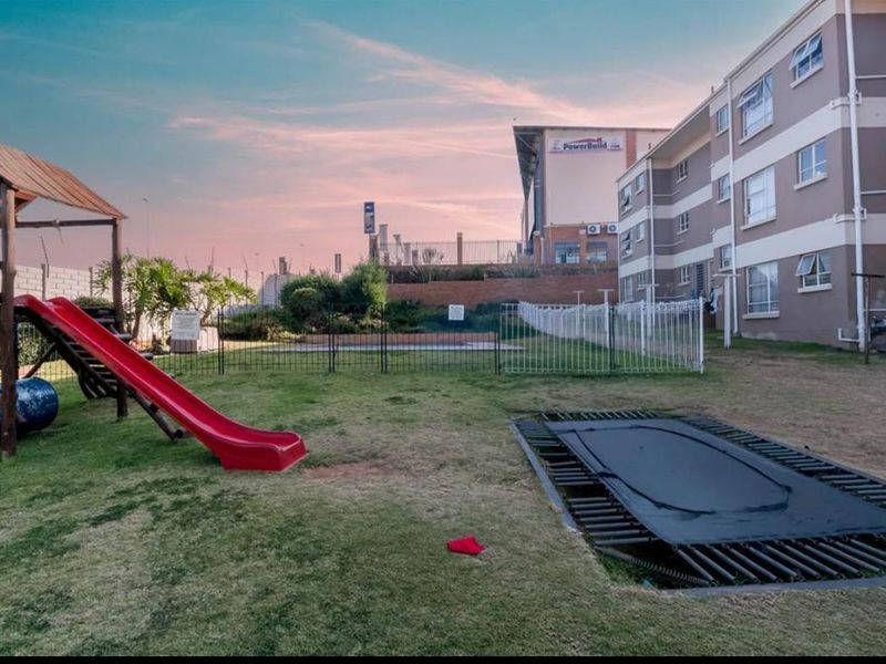Rear exterior view of the townhouse complex featuring a communal garden area with perimeter fencing and a retaining wall.