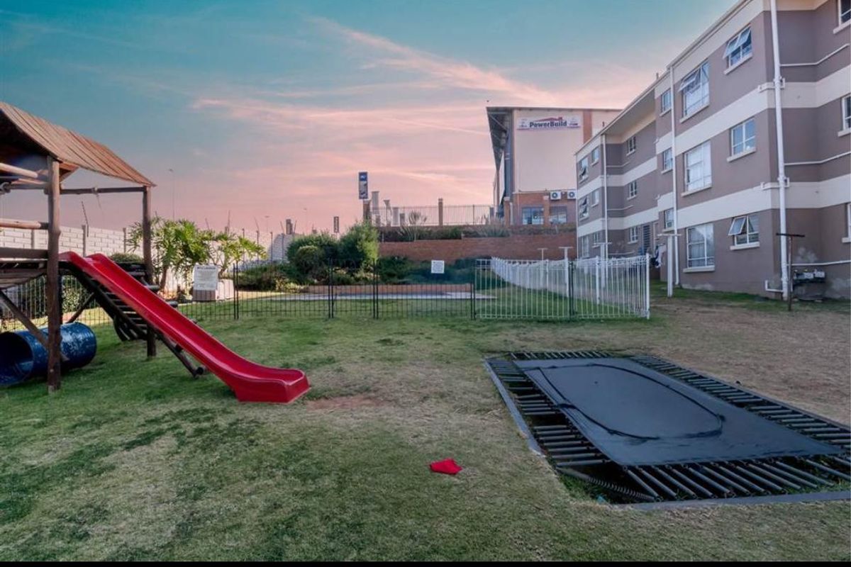 Rear exterior view of the townhouse complex featuring a communal garden area with perimeter fencing and a retaining wall.