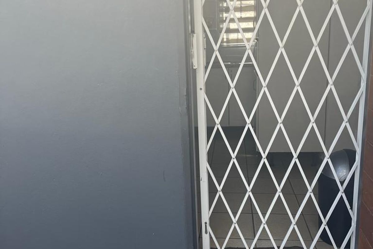 Exterior view of a doorway featuring a white security gate, tiled flooring, and a grey painted wall finish.