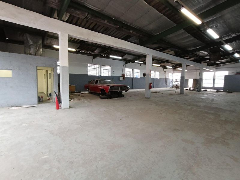 Spacious industrial utility area featuring exposed steel roof trusses, concrete flooring, and functional fluorescent lighting, suitable for workshop or storage use.