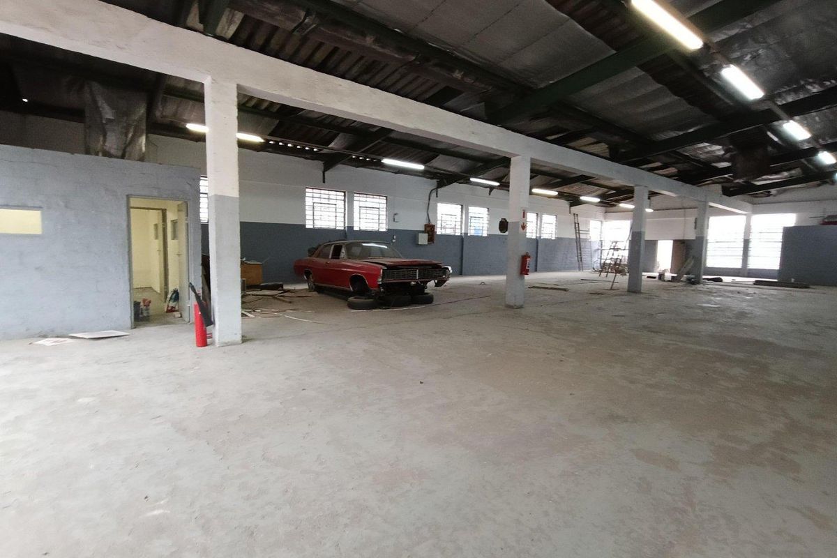 Spacious industrial utility area featuring exposed steel roof trusses, concrete flooring, and functional fluorescent lighting, suitable for workshop or storage use.