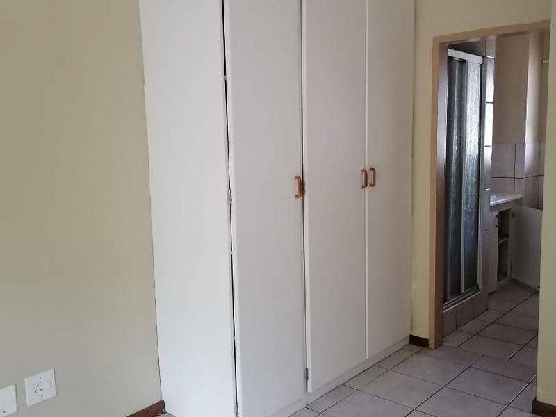 A simple bedroom featuring tiled flooring and a built-in wardrobe, with direct access to an adjacent bathroom area.